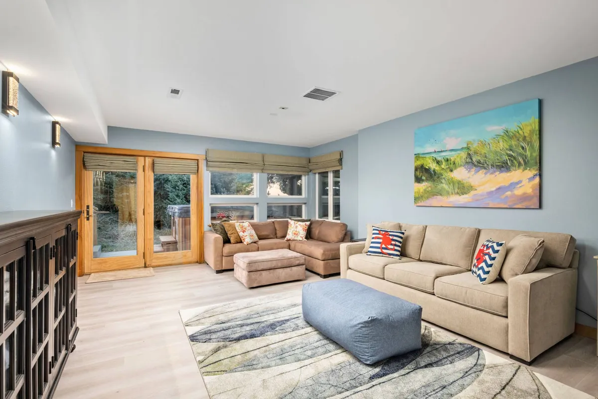 A spacious, welcoming interior living area with a sofa set, large windows, artwork, and sliding doors that hint at easy access to the outdoors. The scene feels both comfortable and connected to the environment beyond the glass.