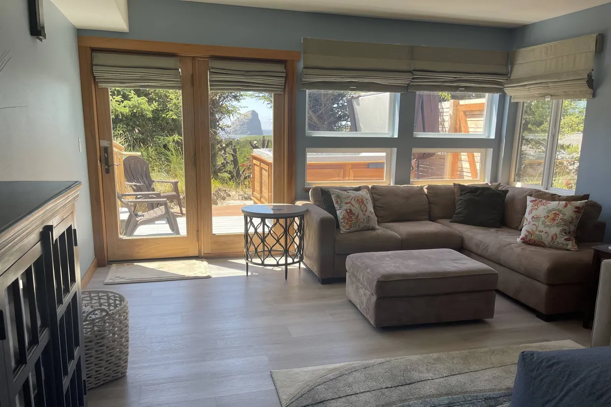 A comfortable and welcoming seating area with large windows offering unobstructed views of the outdoors. The sofa, coffee table, and decorative pillows invite relaxation and intimate conversation while the scenic landscape outside is ever-present.
