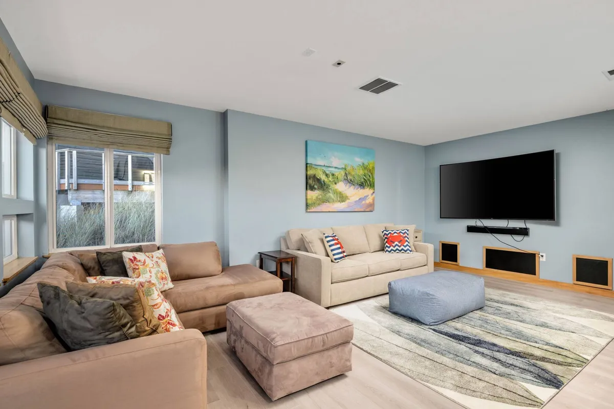 A welcoming family room with a plush couch, vibrant artwork, a large television, and a textured rug. The setup is perfect for both sleeping (with a queen pullout) and entertainment, inviting moments of relaxation or movie nights.