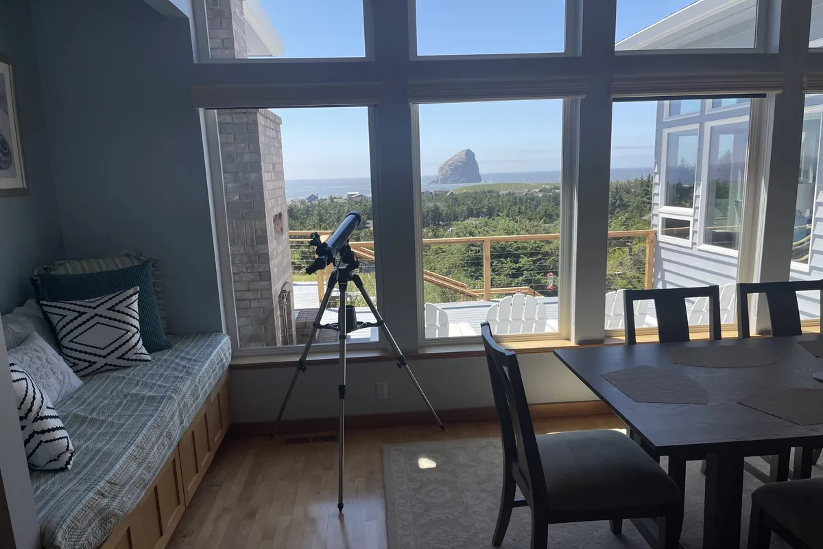 This image features a telescope beside a window with inviting bench seating, suggesting a space for both quiet reflection and active observation of the natural world. The scene is bathed in natural light and framed for family gatherings or solo contemplation.