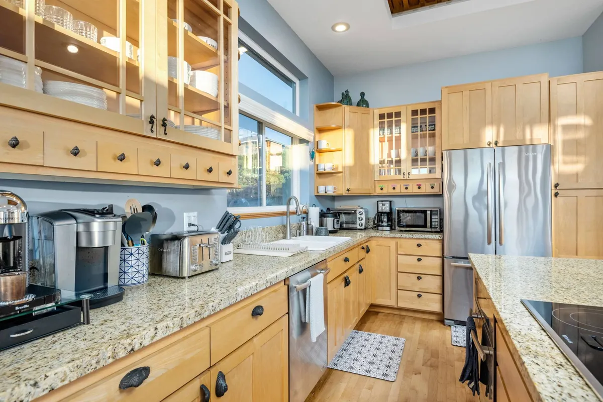 A well-lit chef’s kitchen with elegant granite countertops, wood cabinetry, modern appliances, and ample natural light streaming through the windows. The setting is perfect for crafting gourmet meals and entertaining guests.