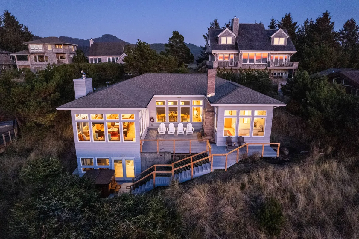 A wide view of the deck with its ample seating, large windows, and natural surroundings. The deck is set for relaxation, sunset views, and gatherings, with enough space for outdoor dining and enjoying ocean breezes.