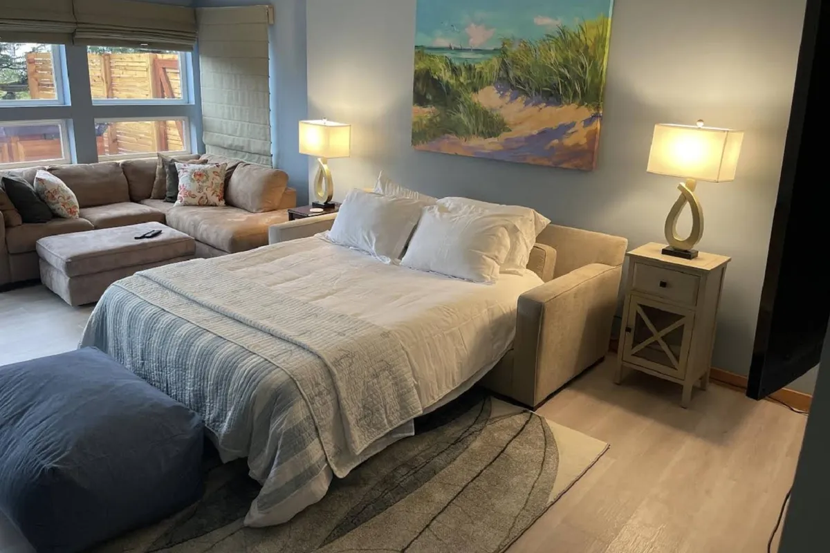 A cozy guest bedroom featuring a comfortable bed, a soft sofa, artistic touches on the walls, and gentle, ambient lighting from table lamps. The room exudes warmth and tranquility, ideal for guests seeking restful nights.